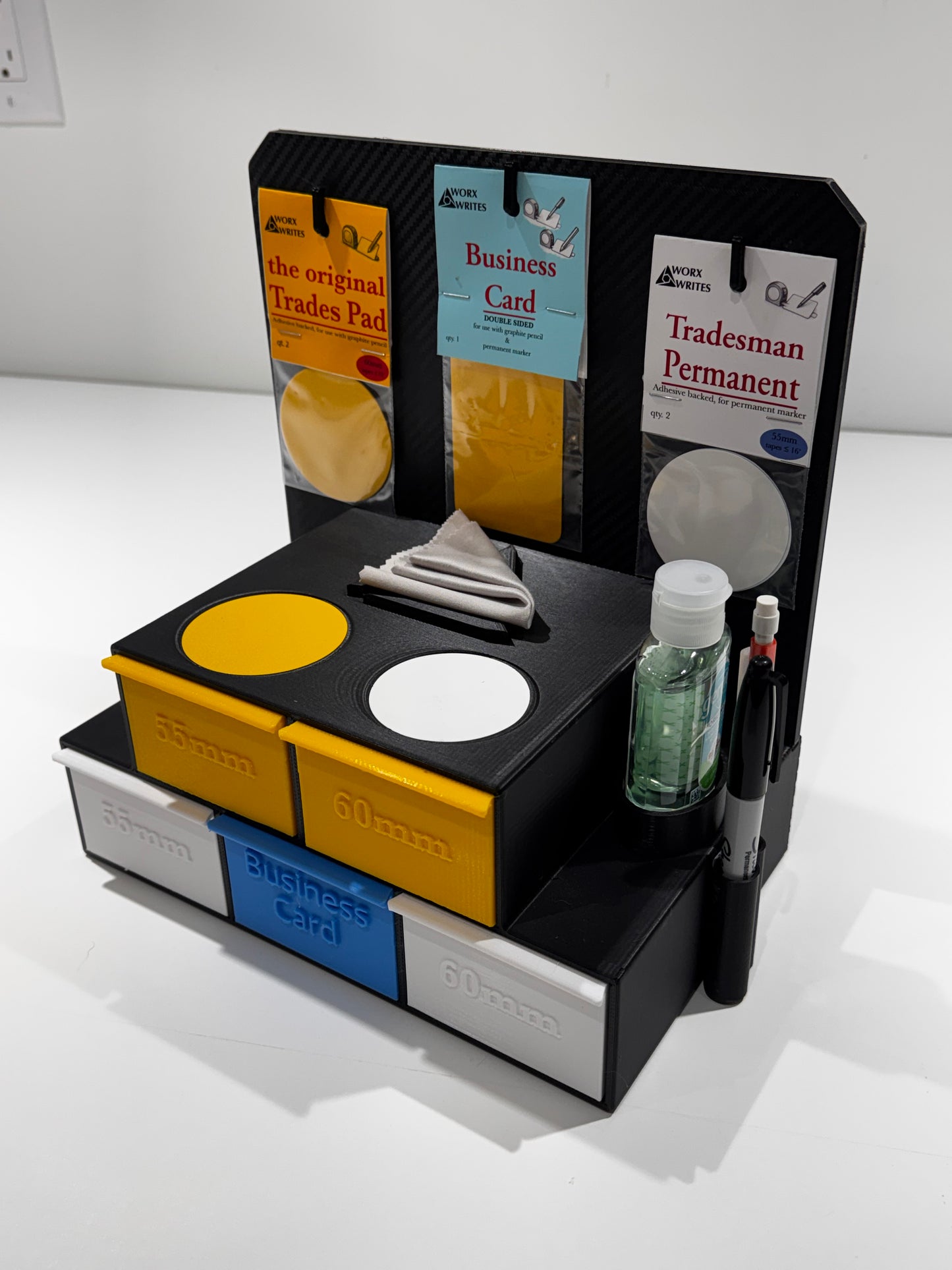 Retail soft start kit display angled view of black stand with compartments holding yellow, white, and blue pads, packaged cards, a marker, and a bottle, on a white surface.