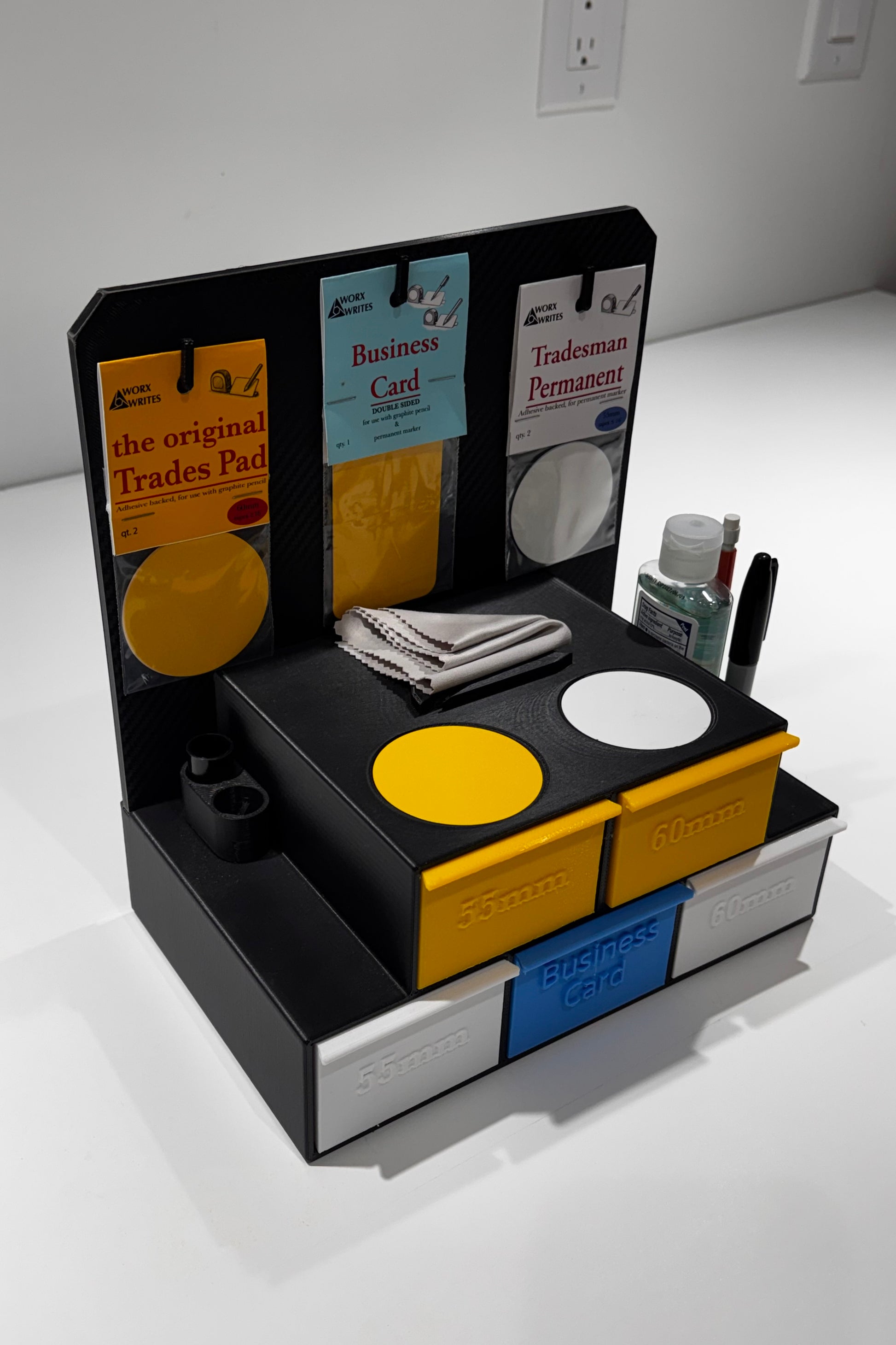 Interactive retail display kit showing an assembled Worx Writes showcase with black stand and compartments holding yellow and blue pads and packaged products, on a white counter.