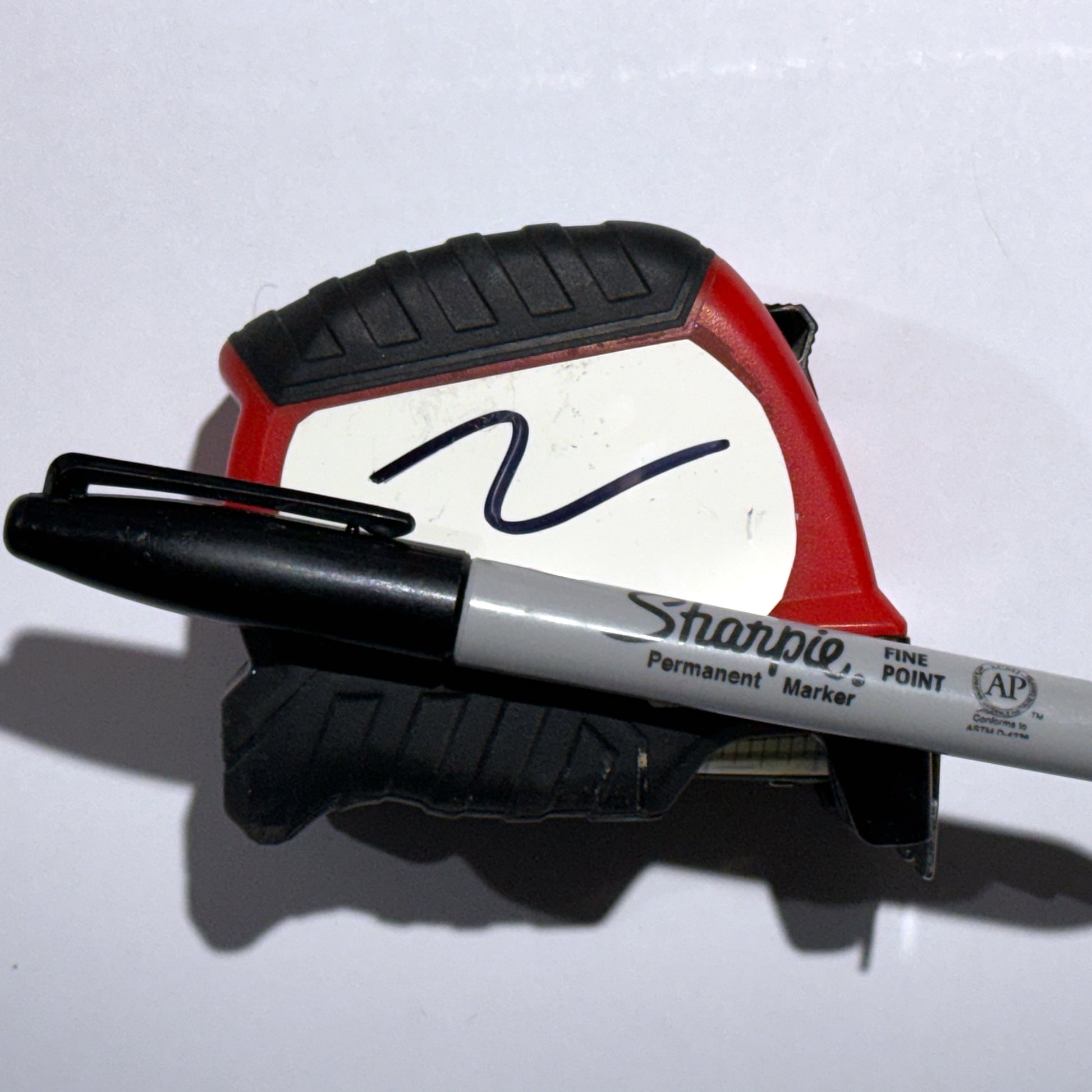 Black Sharpie permanent marker resting on a tape measure with white pad showing scribble, on white background