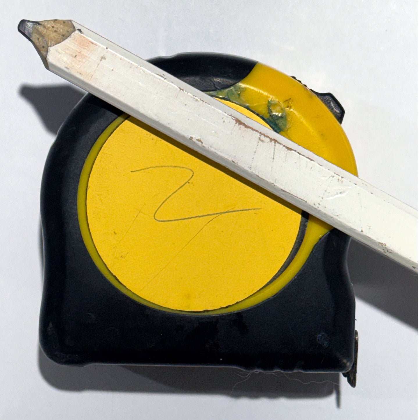 Yellow tape measure pad on black square with a white graphite pencil across the pad on a white background.